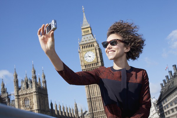 Smiling woman taking self-portrait with digital camera below Big Ben clocktower